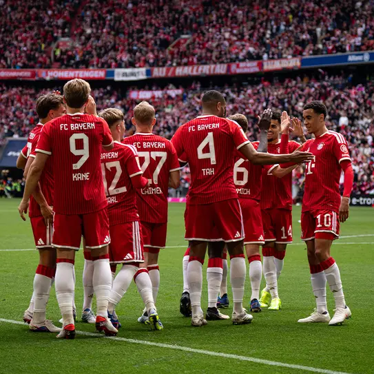 A Bayern München csapatának tagjai ünneplik a gólt, piros mezben láthatók, háttérben szurkolók a stadionban.