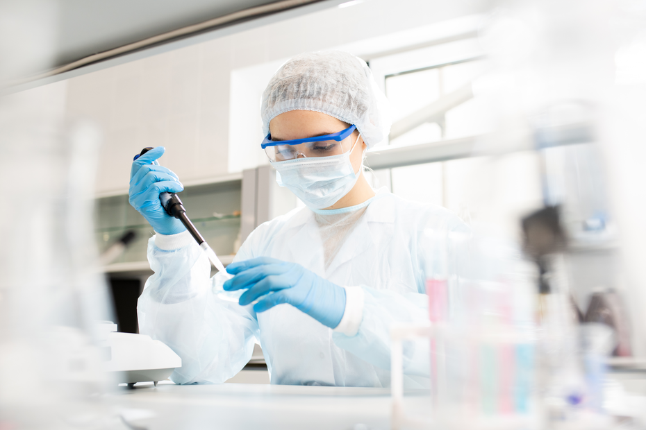 Egy laboratóriumban dolgozó kutató, aki pipettát használ. A nő védőfelszerelést visel, beleértve az arcvédőt és kesztyűt. A háttérben laboratóriumi felszerelések láthatók.