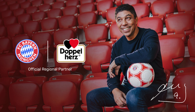 Egy mosolygó férfi ül egy piros stadionszéken, kezében focilabdát tart. A háttérben a Bayern München és a Doppelherz logója látható, mellette az "Official Regional Partner" felirat.